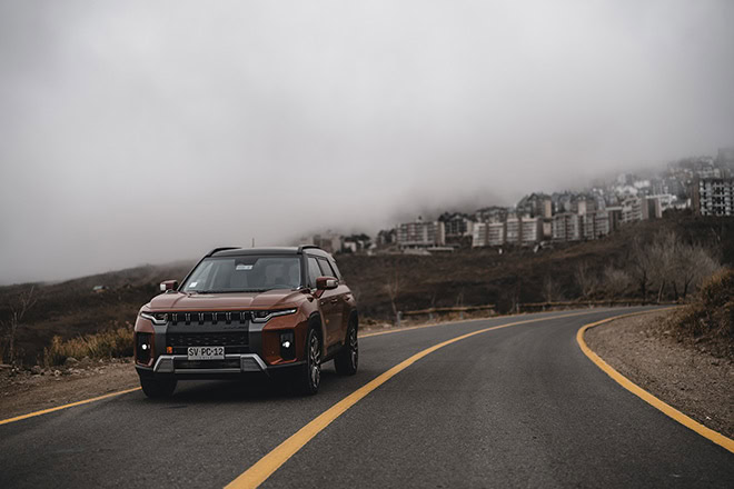 Coche SUV en carretera con ciudad y nubes en el fondo.