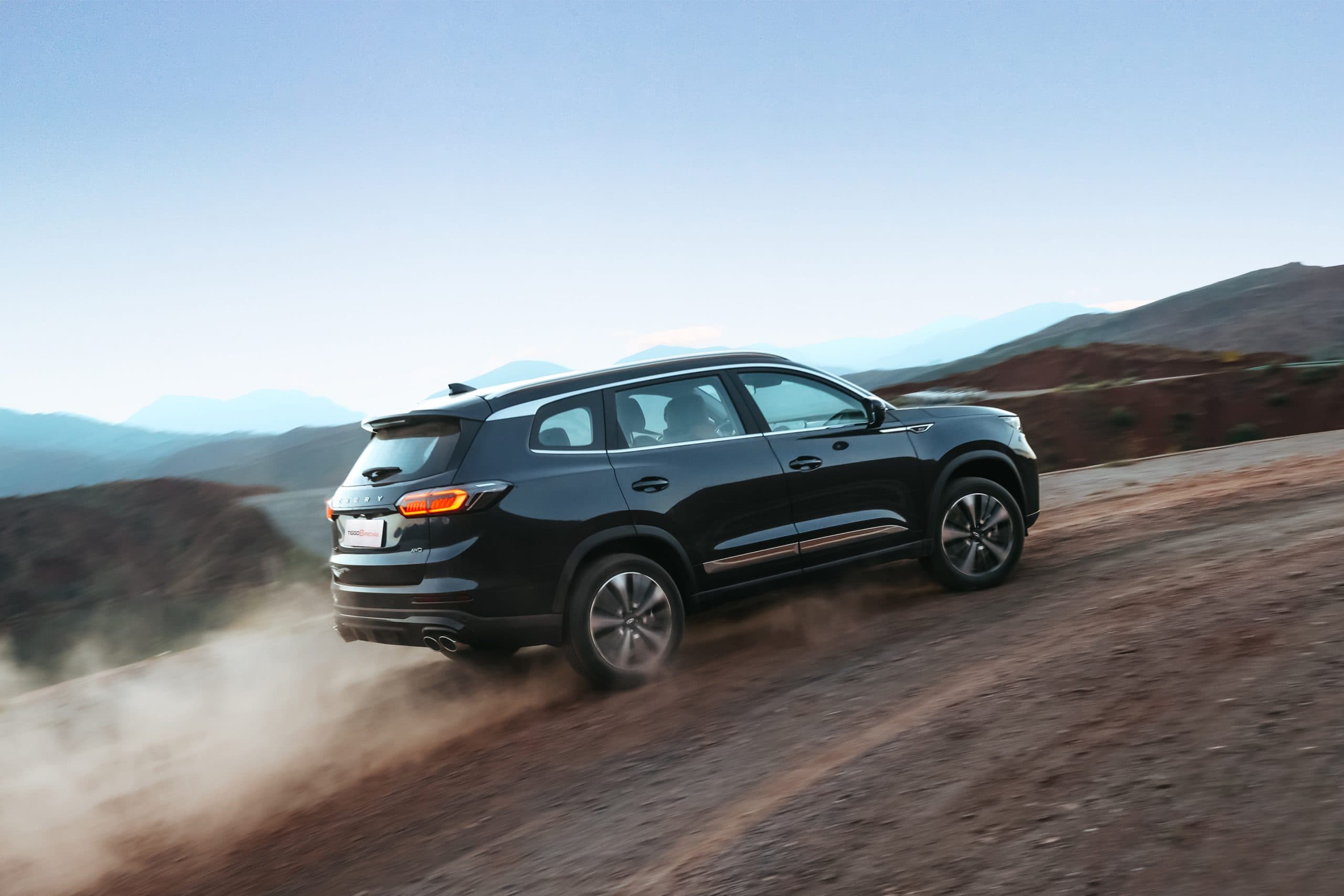 Coche SUV negro en camino de tierra en un paisaje montañoso.