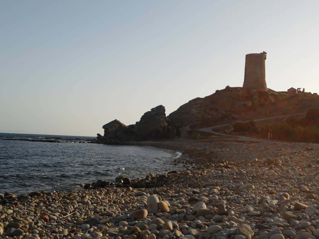 Ancient tower ruins overlooking a pebbled beach at sunset.
