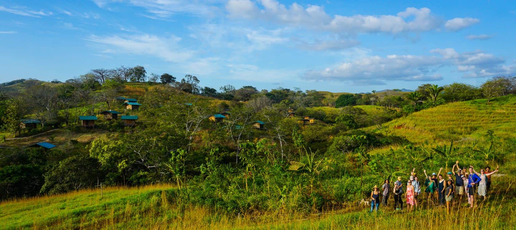Group of people walking and gathering in a green hillside village landscape.