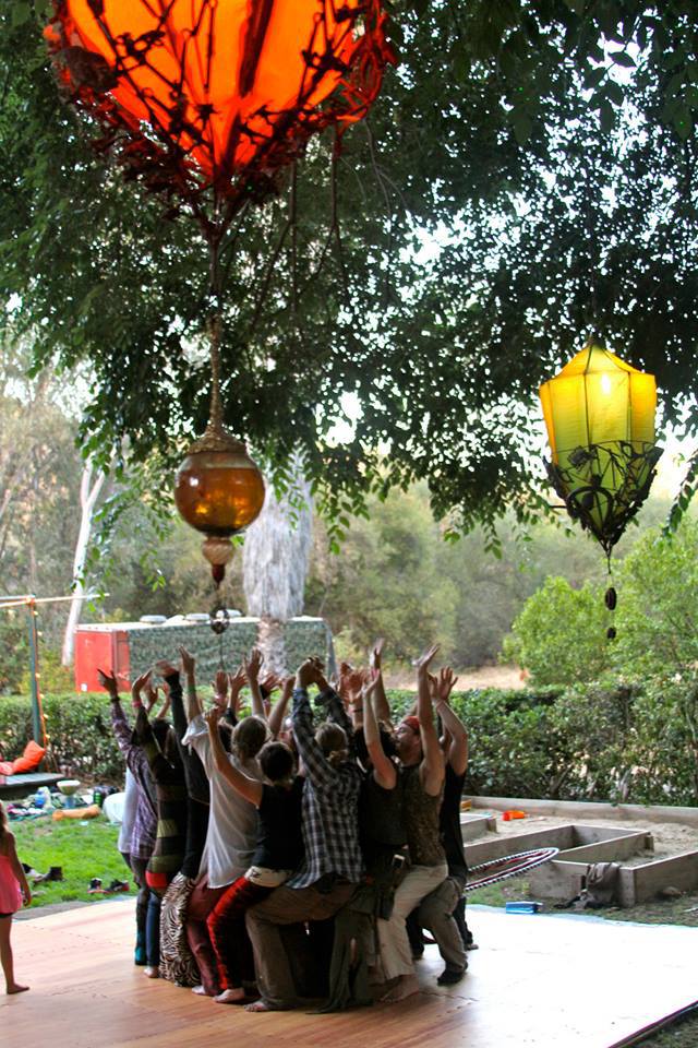 Group of people with raised hands under hanging lanterns in an outdoor courtyard.
