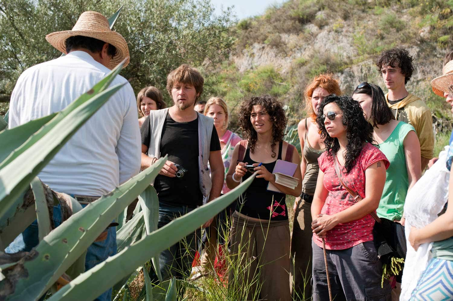 Group of people on an eco village tour listening to a guide in a natural setting.