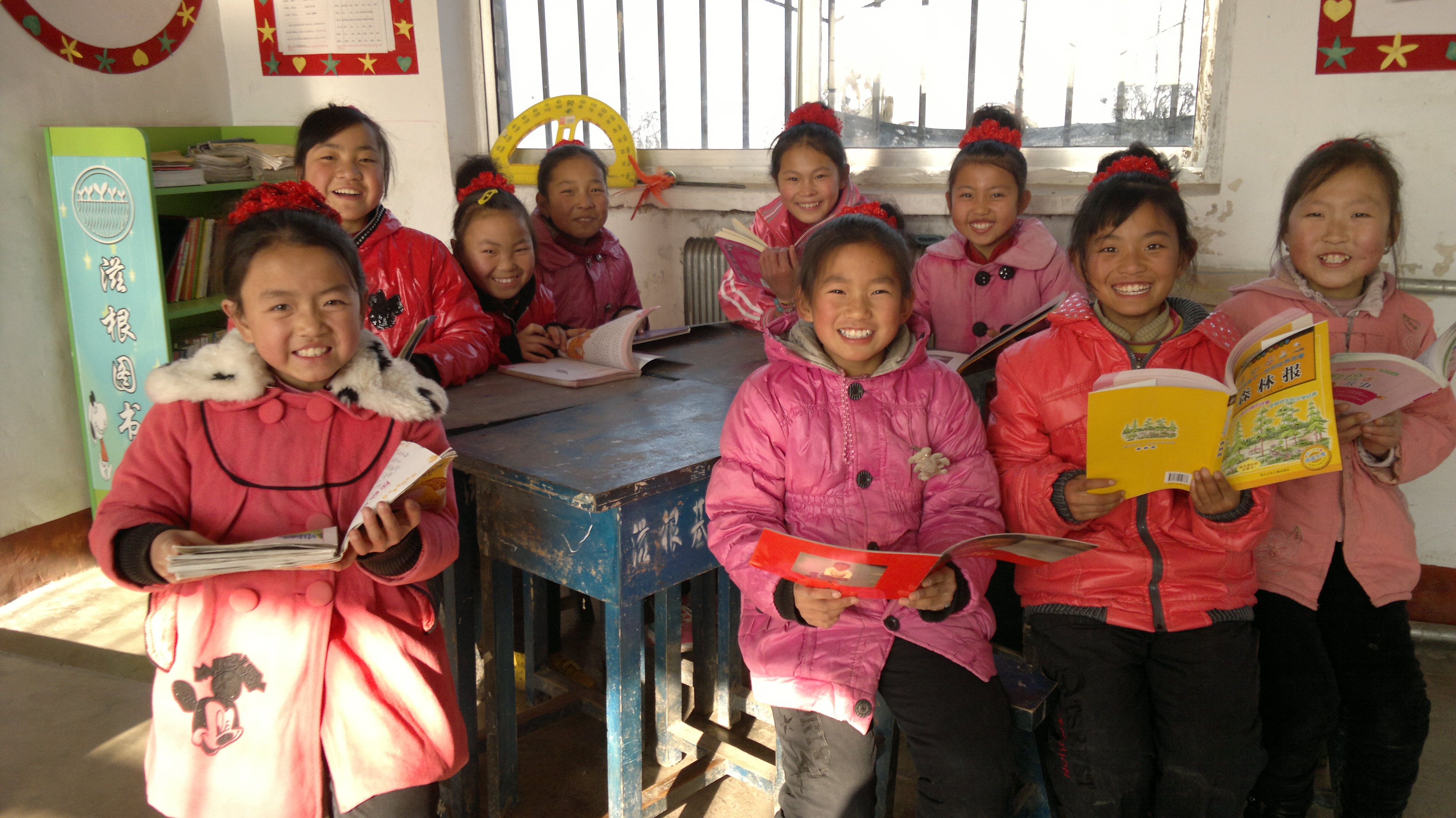 Group of smiling children in pink jackets reading books in classroom.