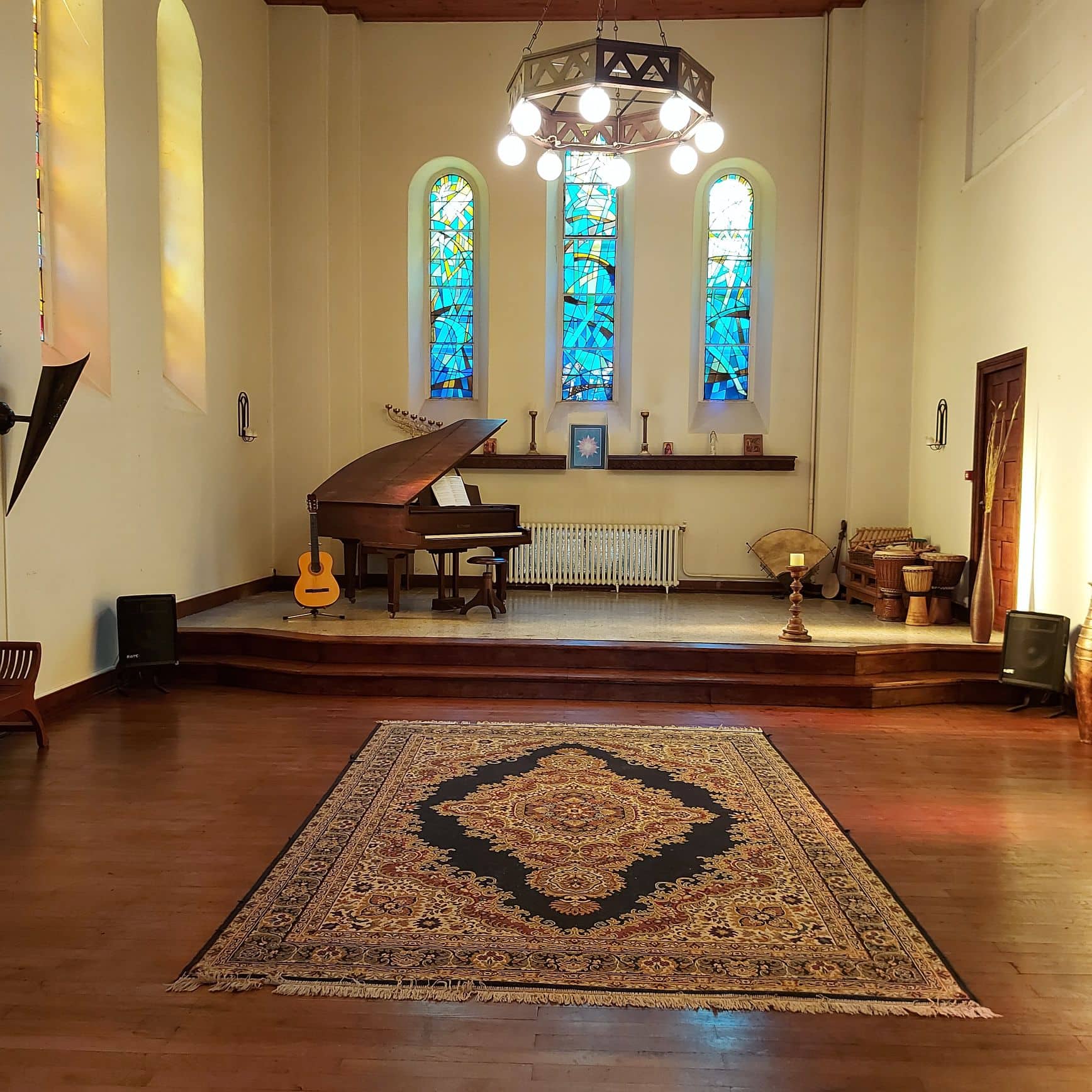 Soothing recital room with grand piano, stained glass windows and rug.