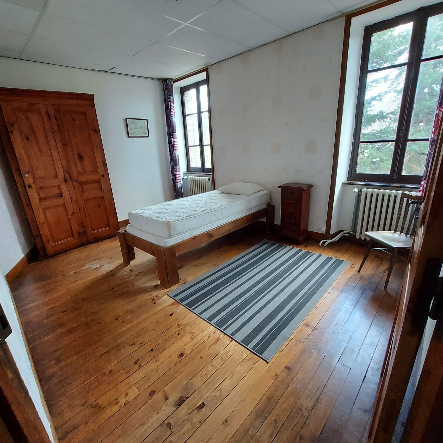 Single bed in a simple rustic bedroom with wooden floor and wardrobe.