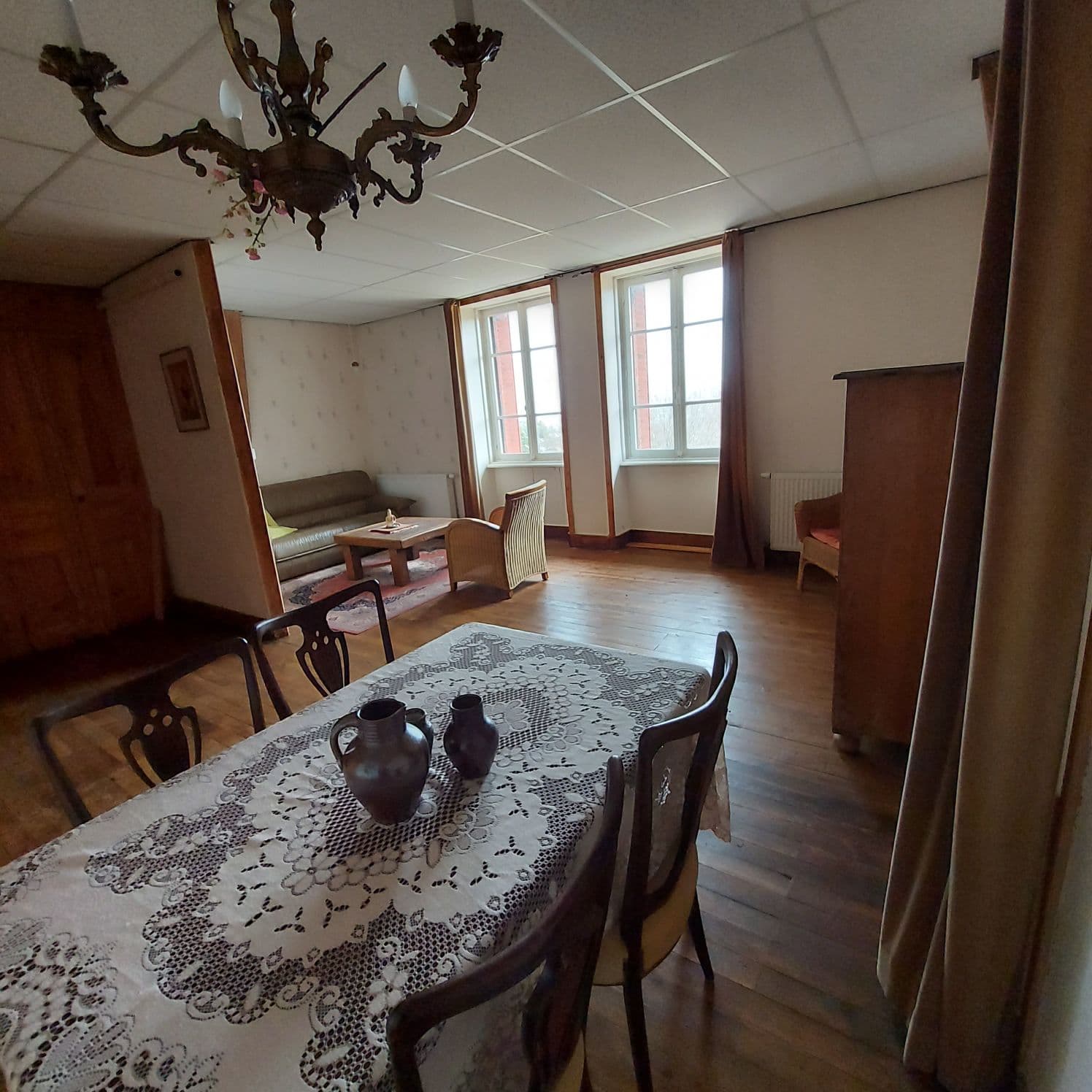 Interior of a vintage living and dining room with a lace tablecloth and wooden furniture.