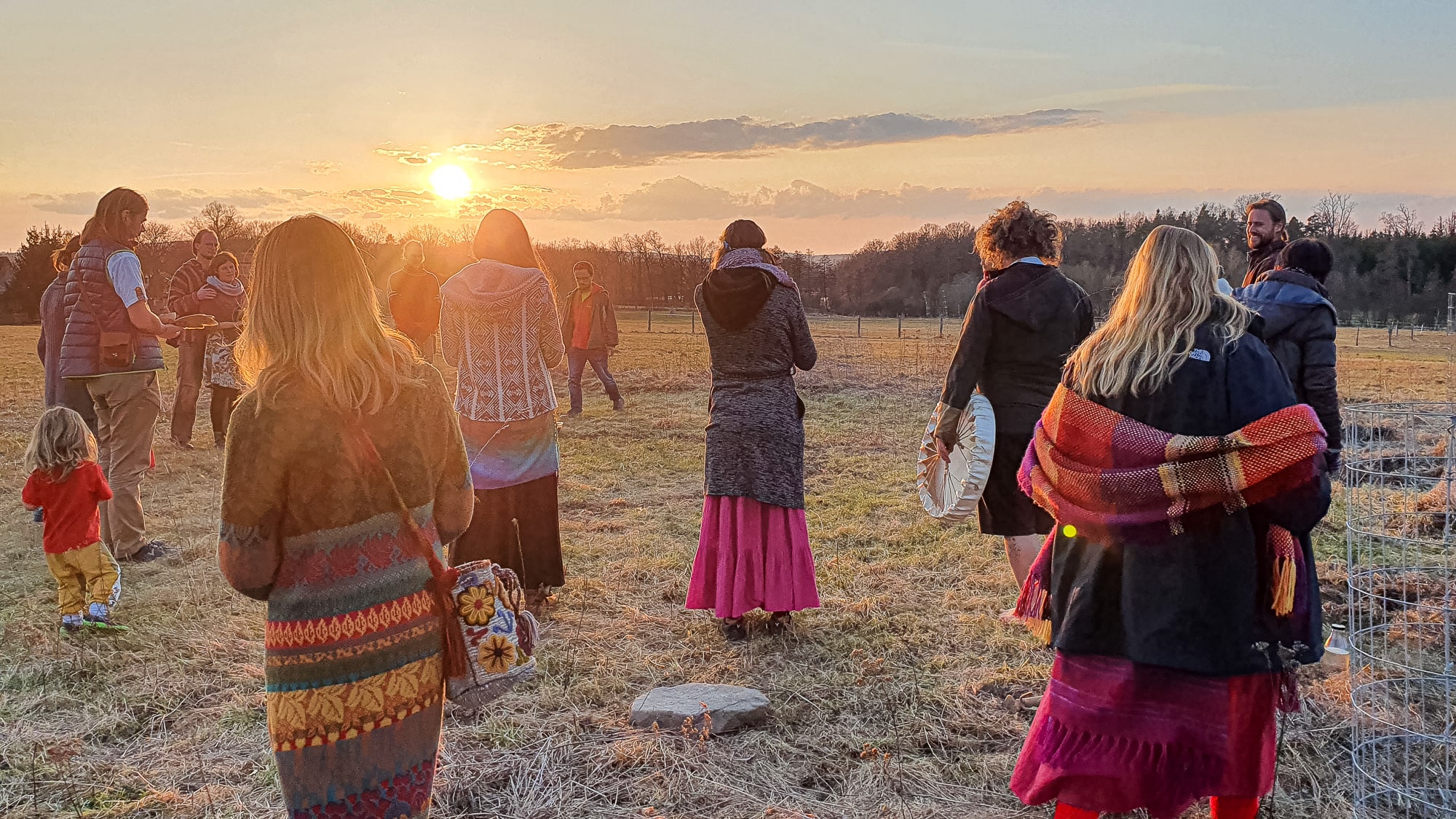 Group of people in a field at sunset, embracing and talking.