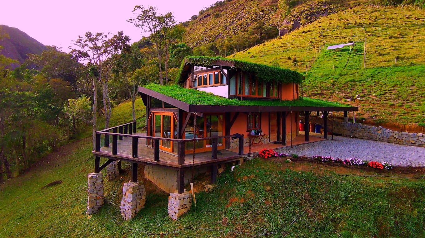 Scenic hillside eco village house on stilts with wooden deck and green roof.