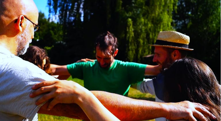 Group of diverse people in a circle holding arms together outdoors.