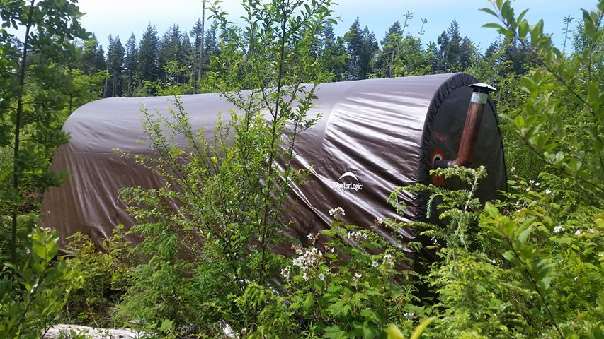 Greenery surrounds a brown flexible shelter structure in a forested area.