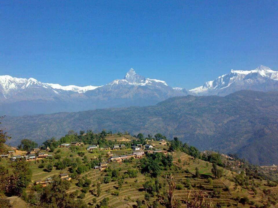 Scenic terraced hillside village with snow-capped mountains in the distance.