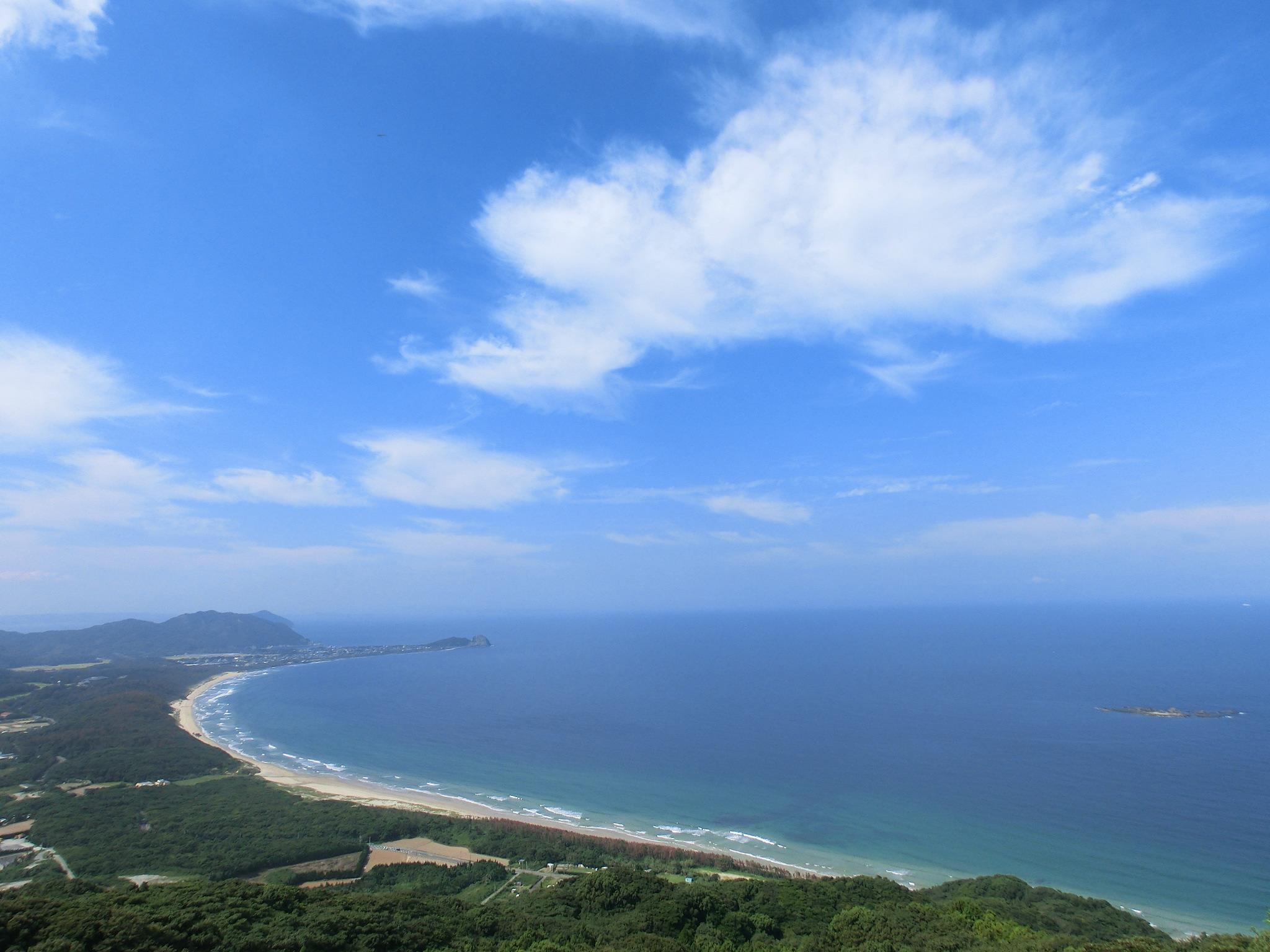 Aerial coastal landscape with blue sky, turquoise sea and curved sandy beach.
