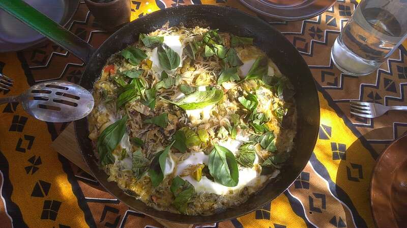 Vibrant dish in a skillet with greens and fried egg, rustic table setting.