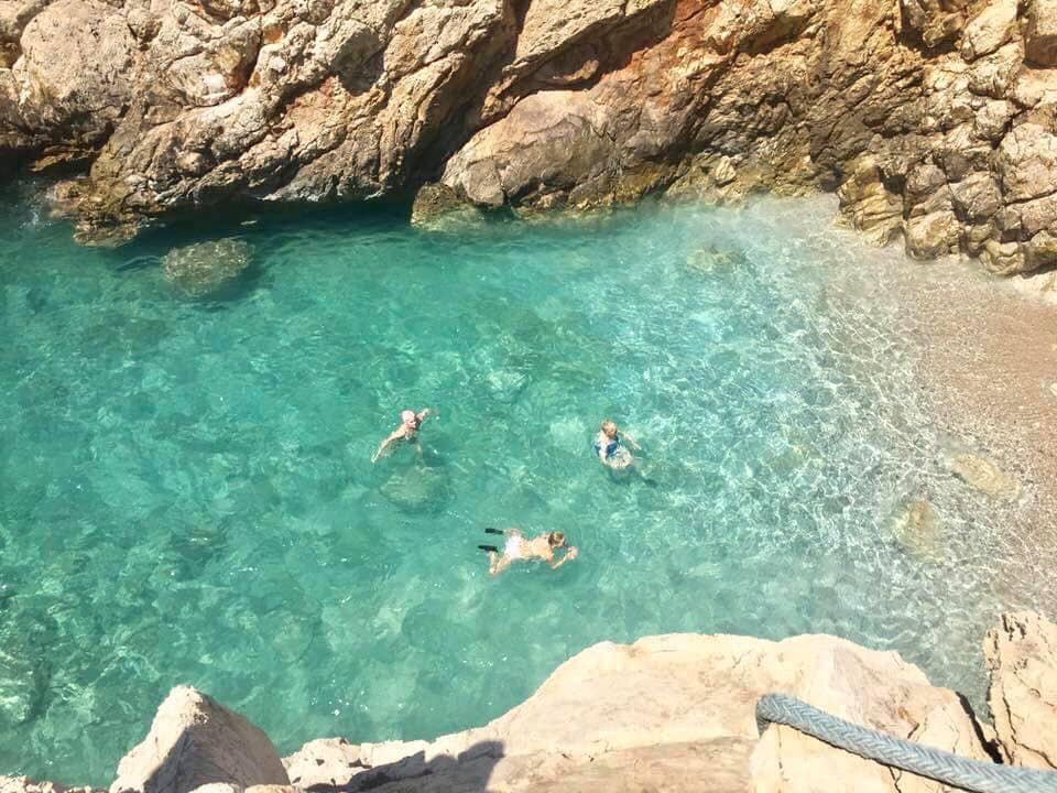Crystal clear turquoise coastal pool with rocky shore and three swimmers.