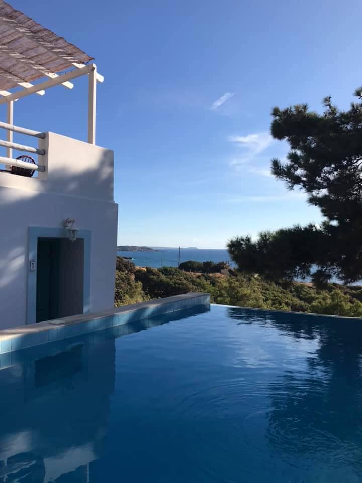 Infinity pool with white building and blue door overlooking the sea.