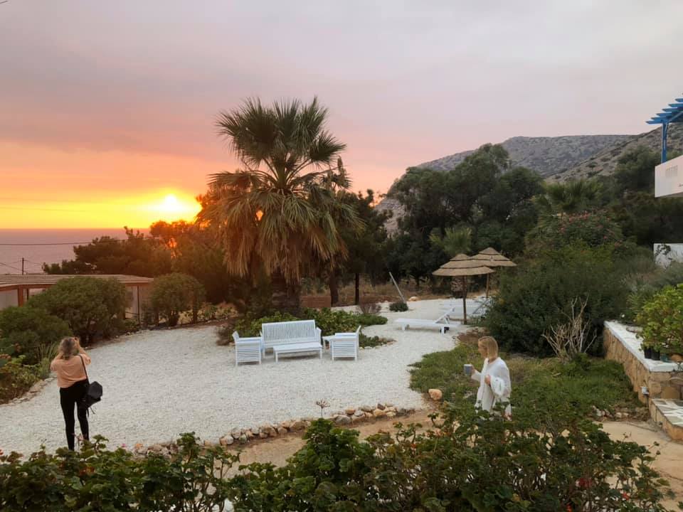 Sunset over a garden and seating area at Kallipoli Ecovillage with palm trees and lounge chairs.
