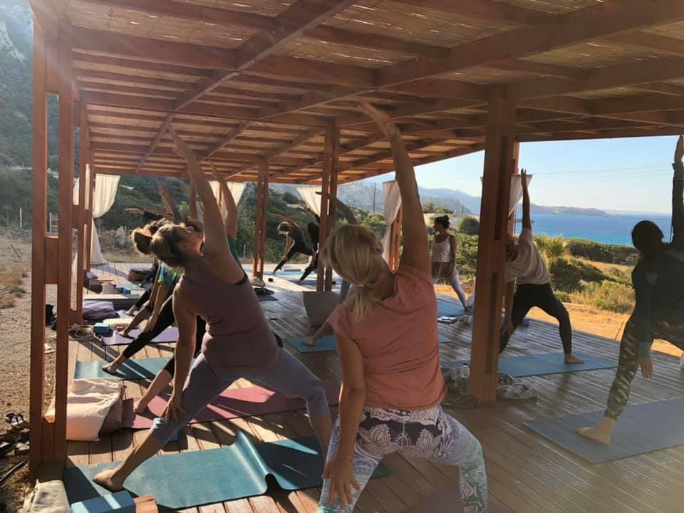 Group of people practicing yoga outdoors under a wooden pavilion with mats.