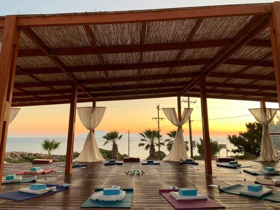 Sunset over a coastal eco village deck with shaded lounging areas and palm trees.