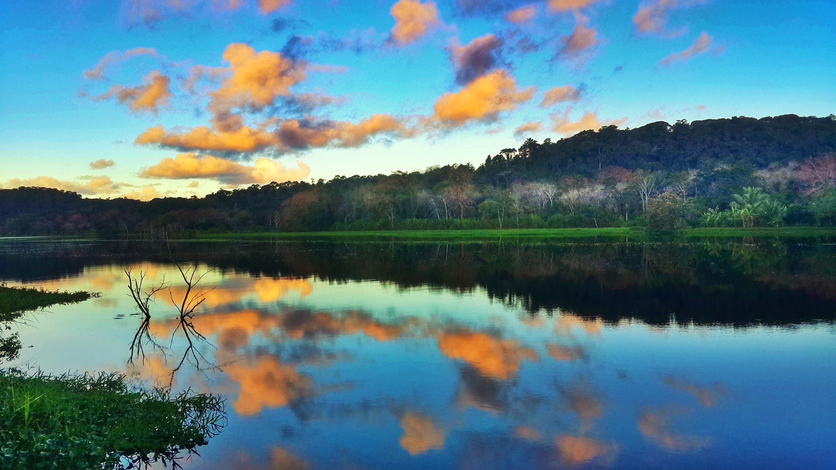 Sunset over calm lake with orange clouds reflected in water.