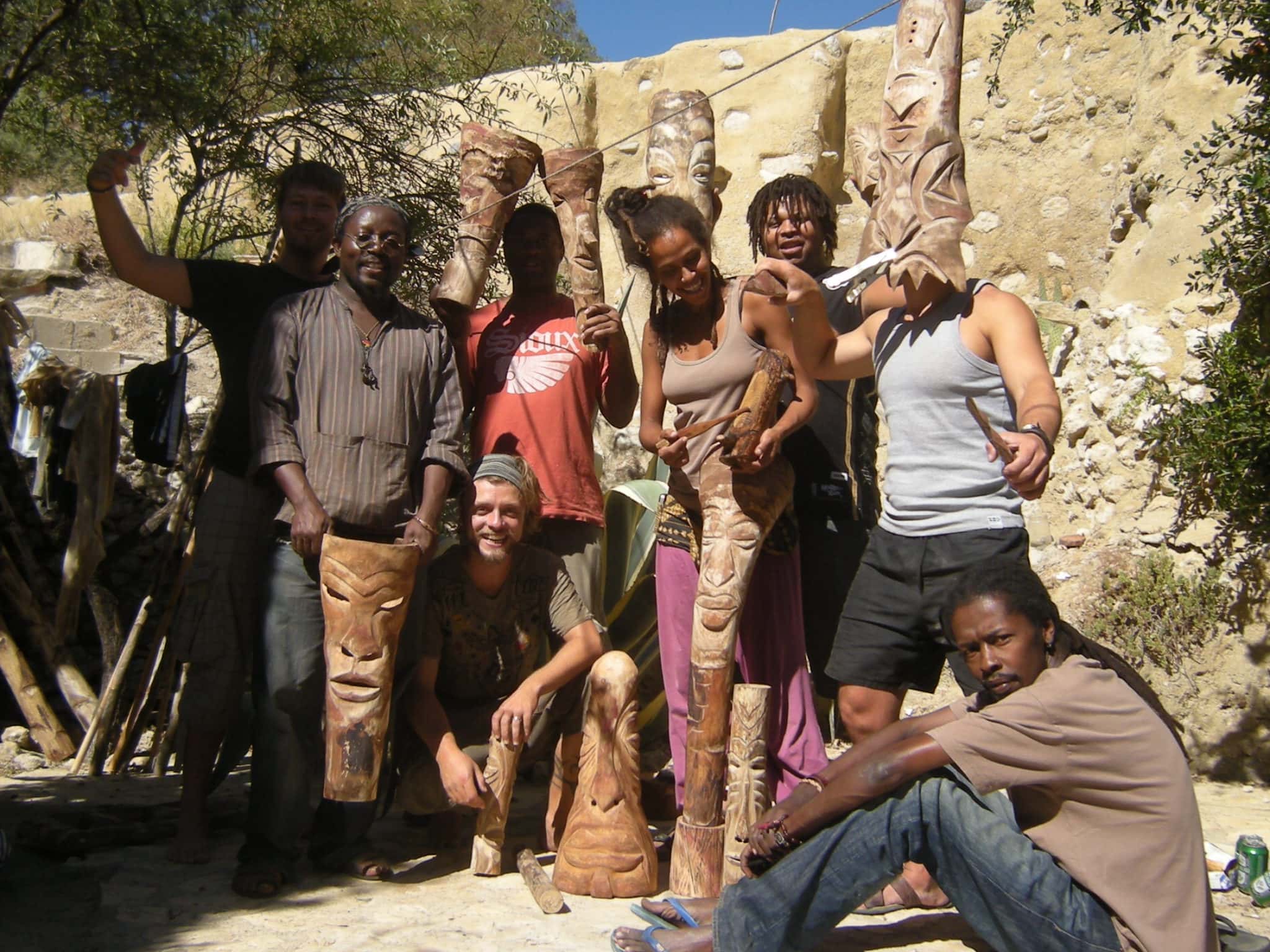 Group of people standing with carved wooden totems in outdoor setting.