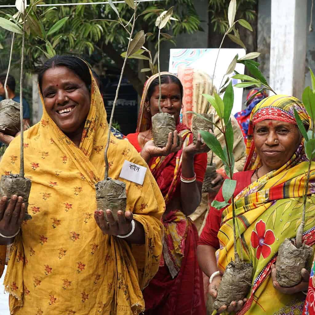 Women holding saplings and clay pots at eco-friendly event in Bangladesh.