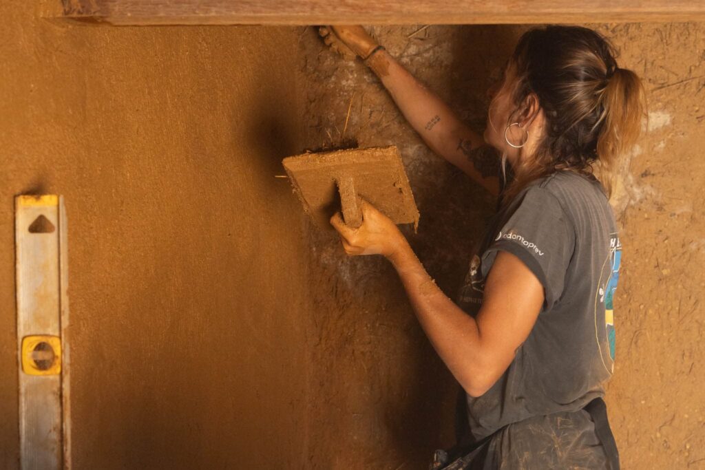 Volunteer woman plastering an earthy wall at an Eco village project.