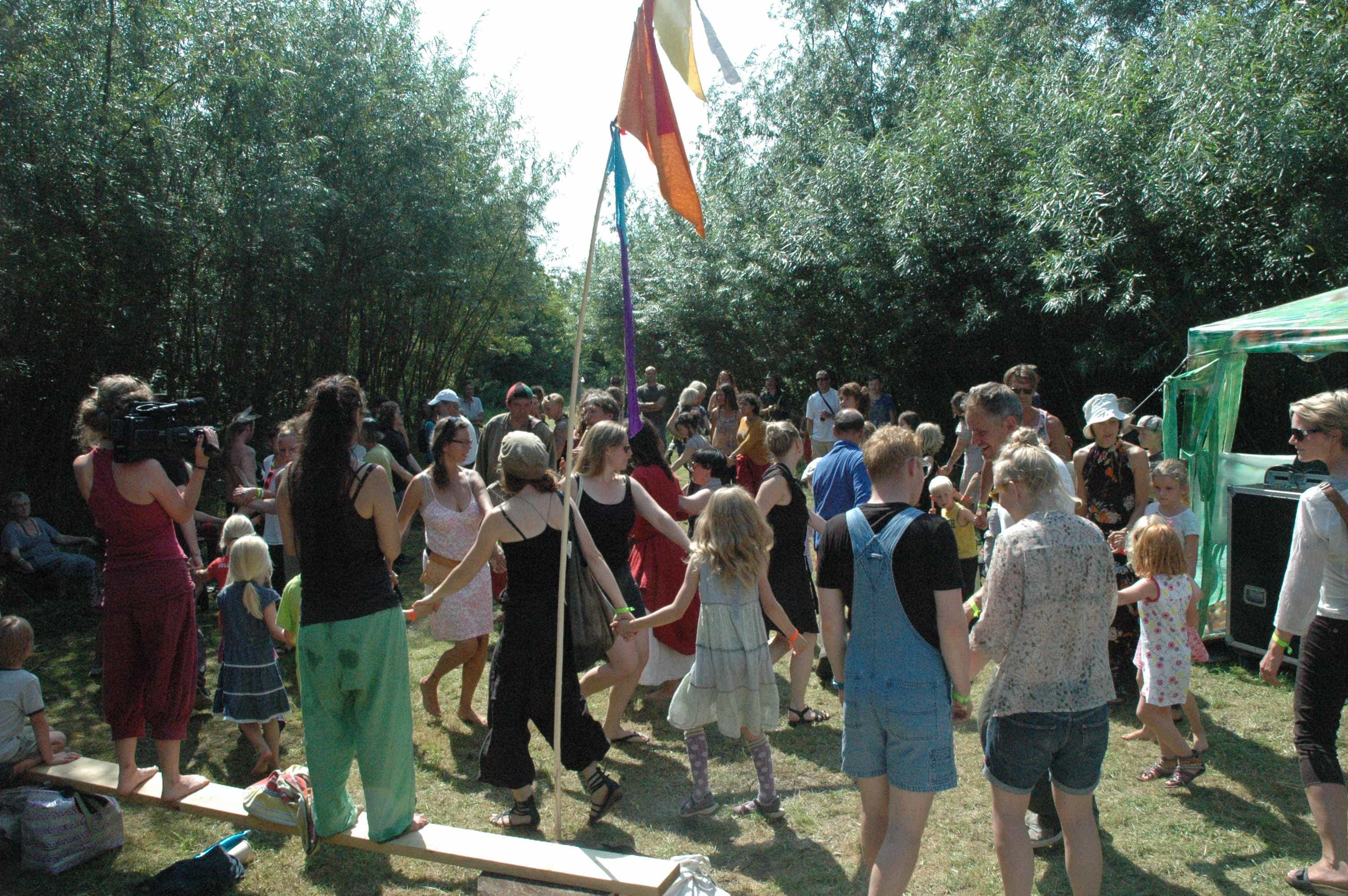 People dancing and socialising at an outdoor eco village gathering in a sunny garden.