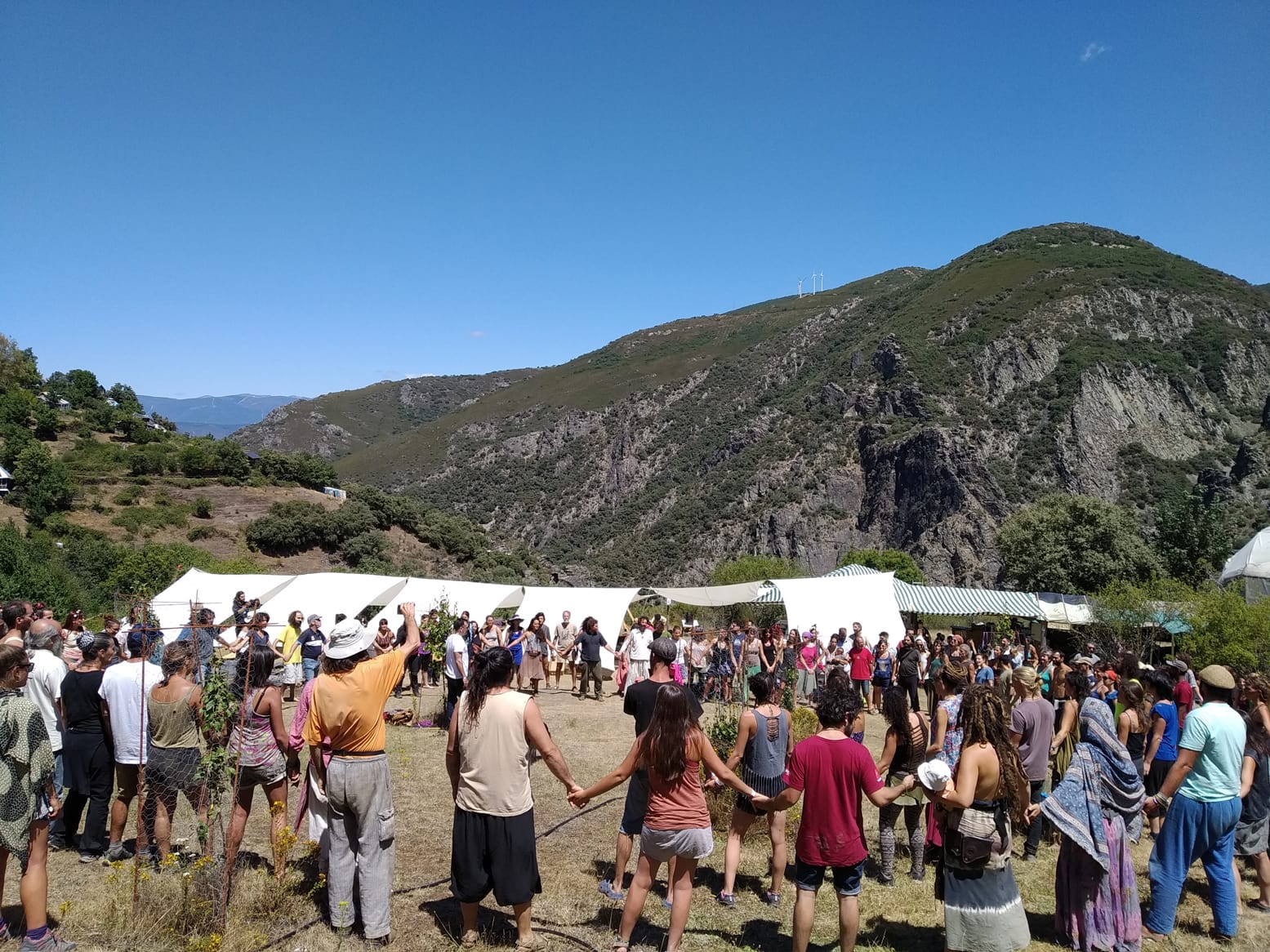 Group of people gathering outdoors with tents in a valley surrounded by mountains.