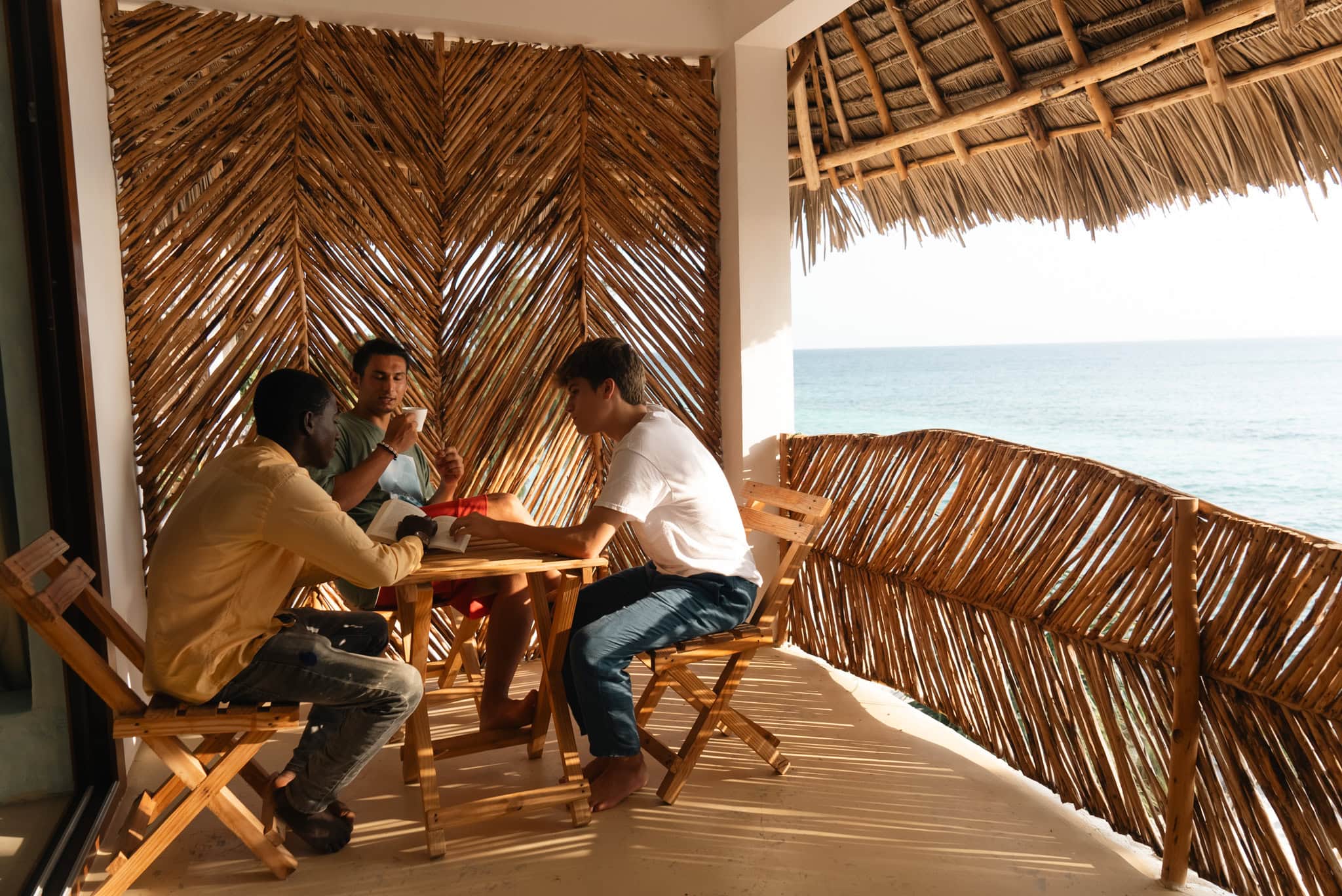People converse at a seaside thatched terrace with the ocean view.