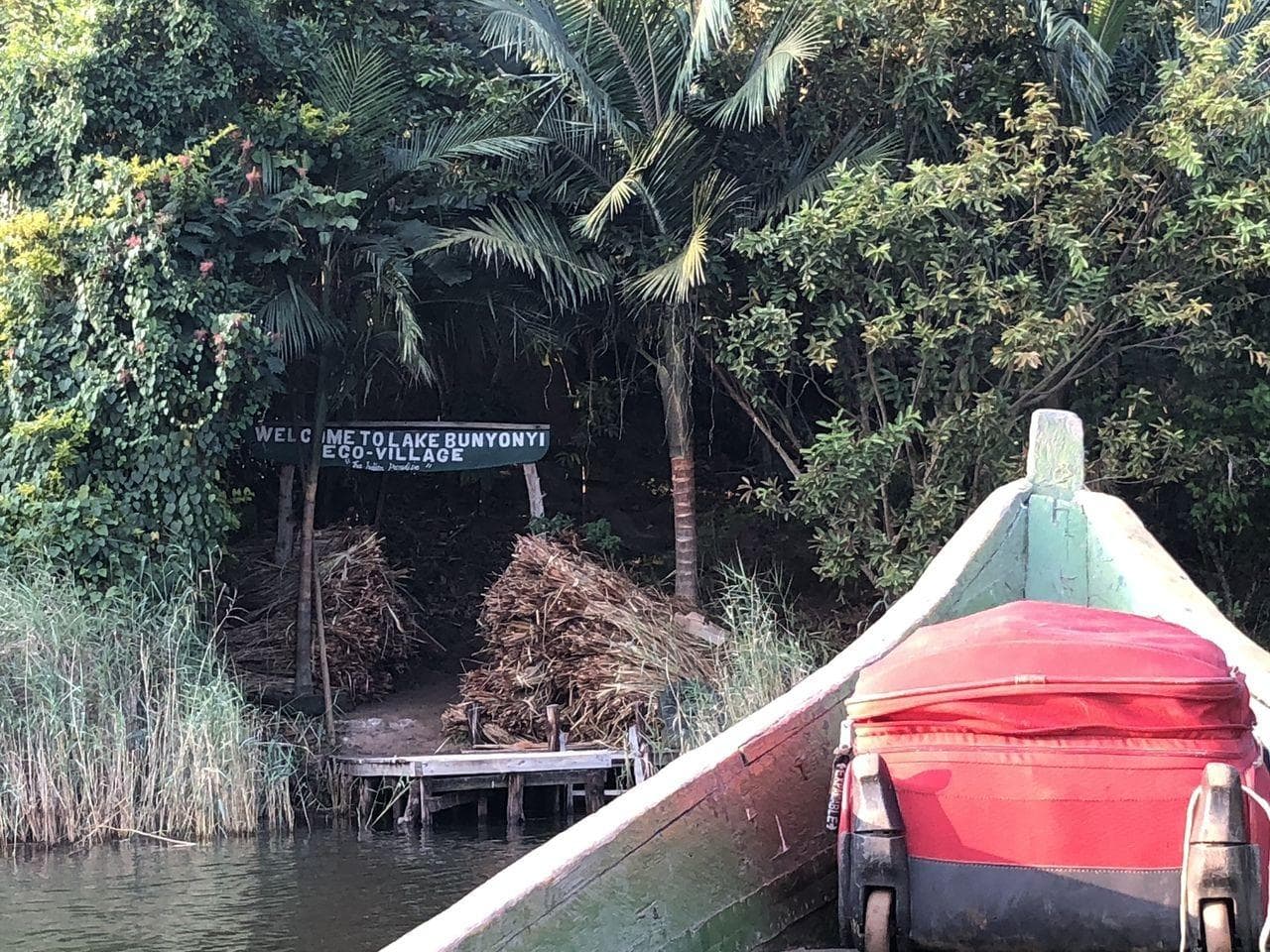 Scenic lakeside ecovillage boardwalk with boat and lush tropical trees.