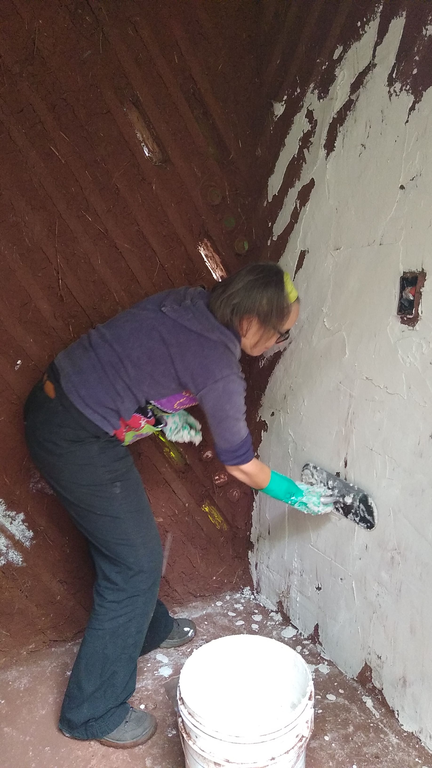 Volunteer applying plaster on a wall at a building site.