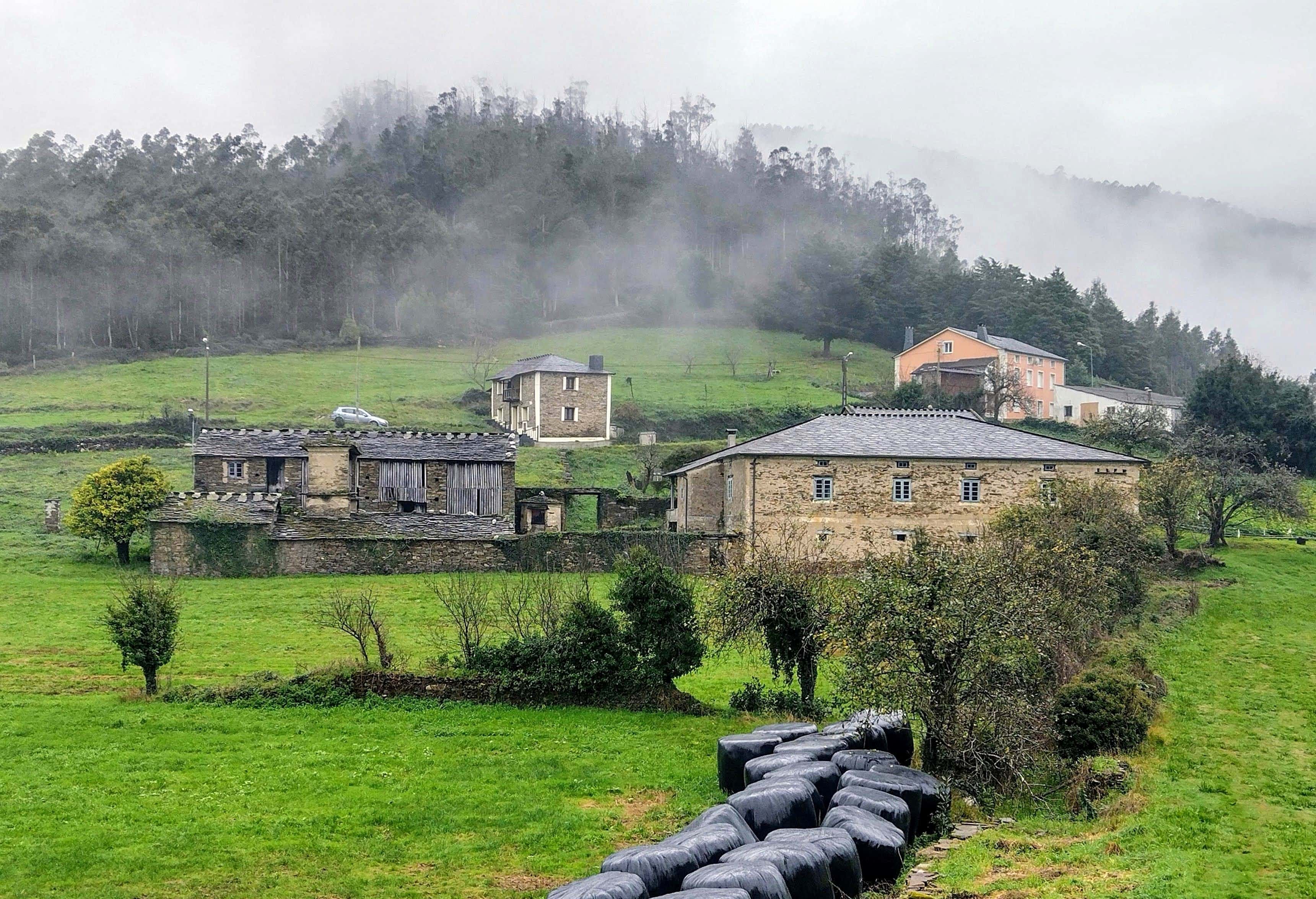Ecological village landscape with stone buildings, green fields and misty hills.