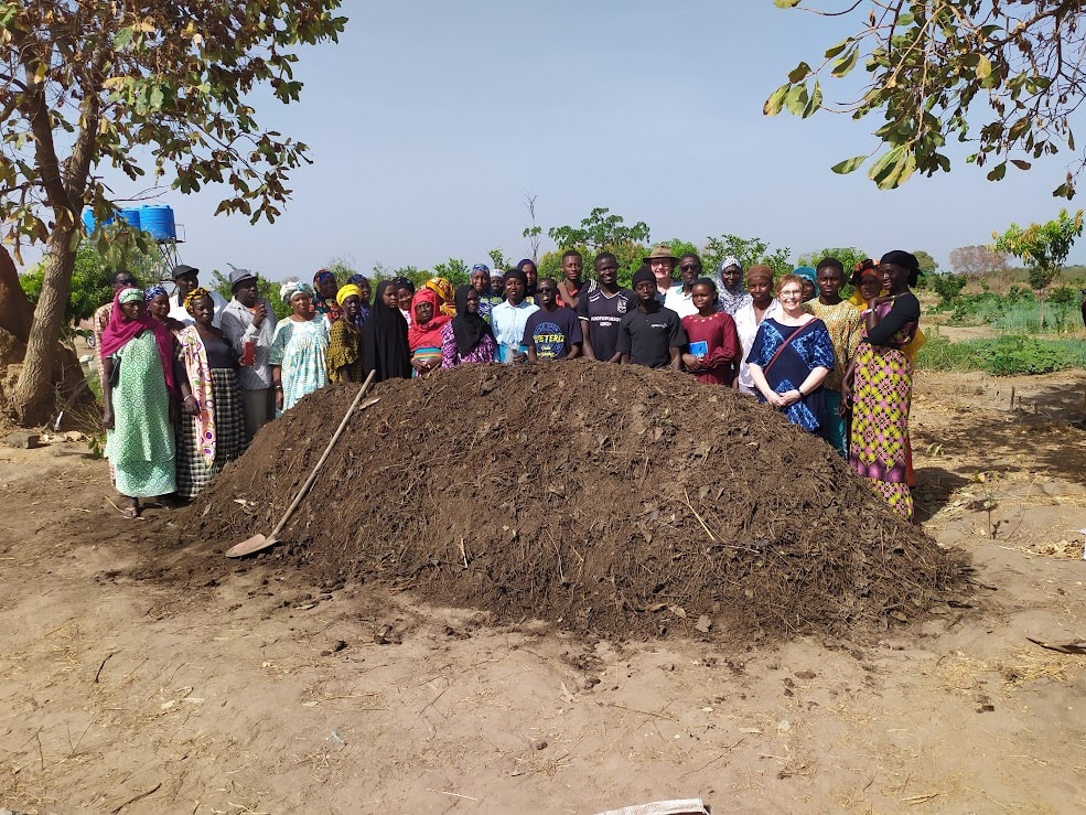 Group photo around a large compost pile at a community project in The Gambia.