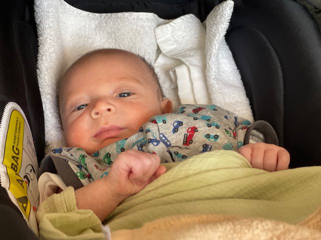 Baby in a car seat with a patterned onesie and blanket.