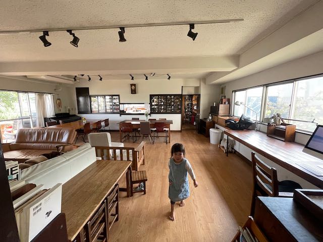 Spacious communal room with wooden furniture and a child walking across the floor.