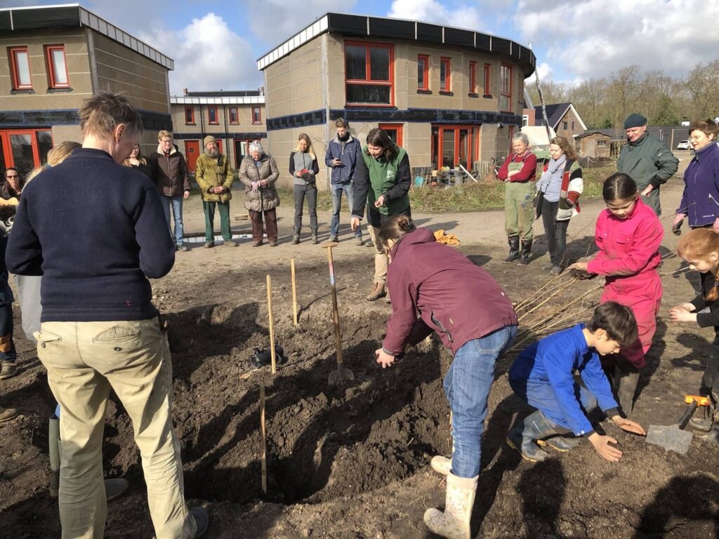 Group of people planting saplings at an ecovillage site.
