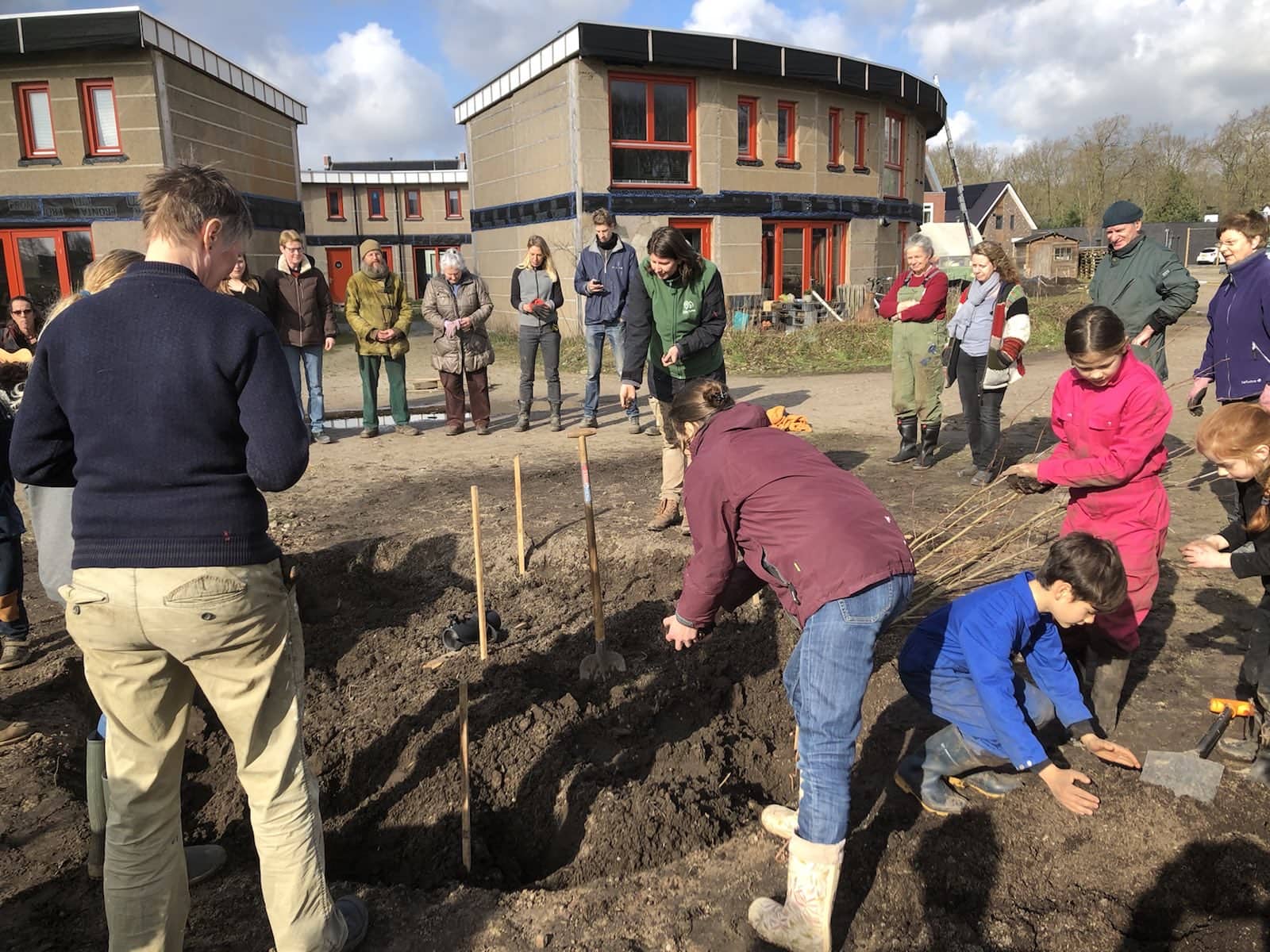 Group of people planting saplings at an ecovillage site.