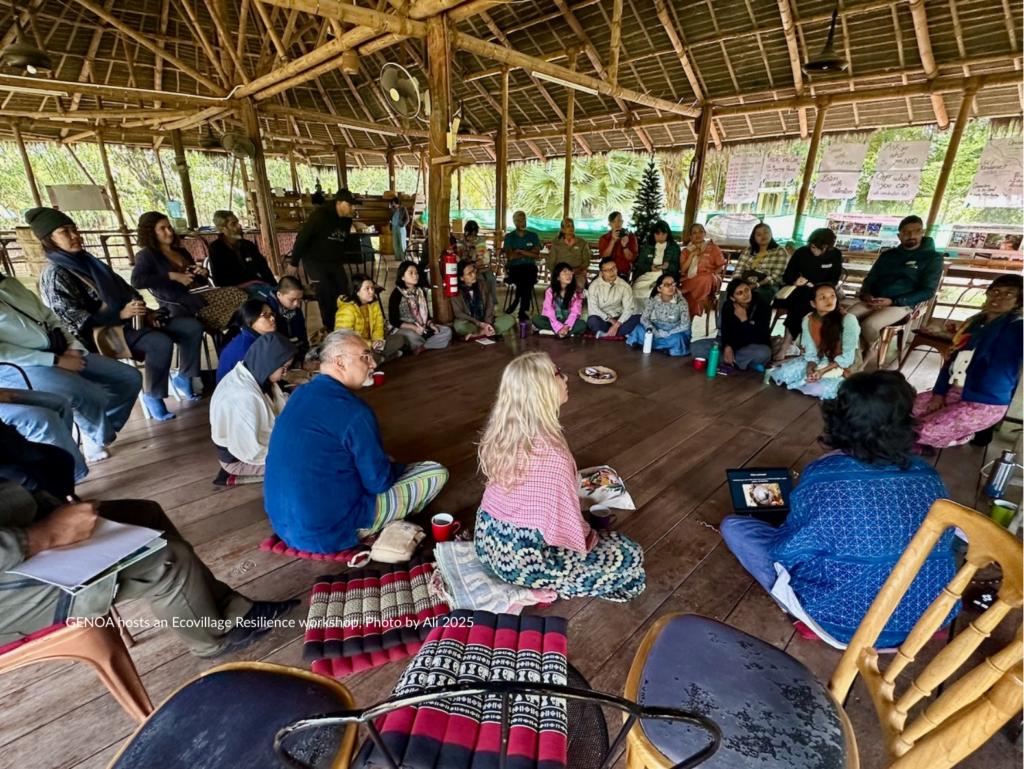 Group of people seated in a circular arrangement inside a rustic open-air structure.