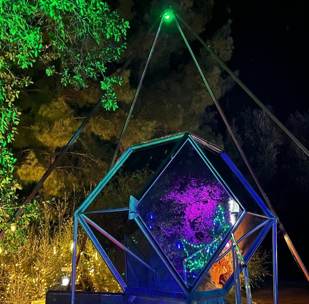 Geometric glass sculpture in night garden with vibrant green and purple lighting.