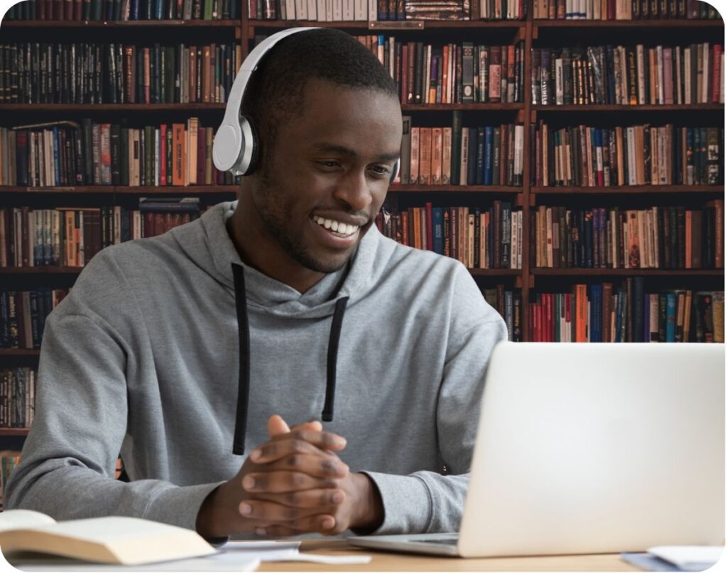 Person wearing headphones using laptop for online learning in library setting.