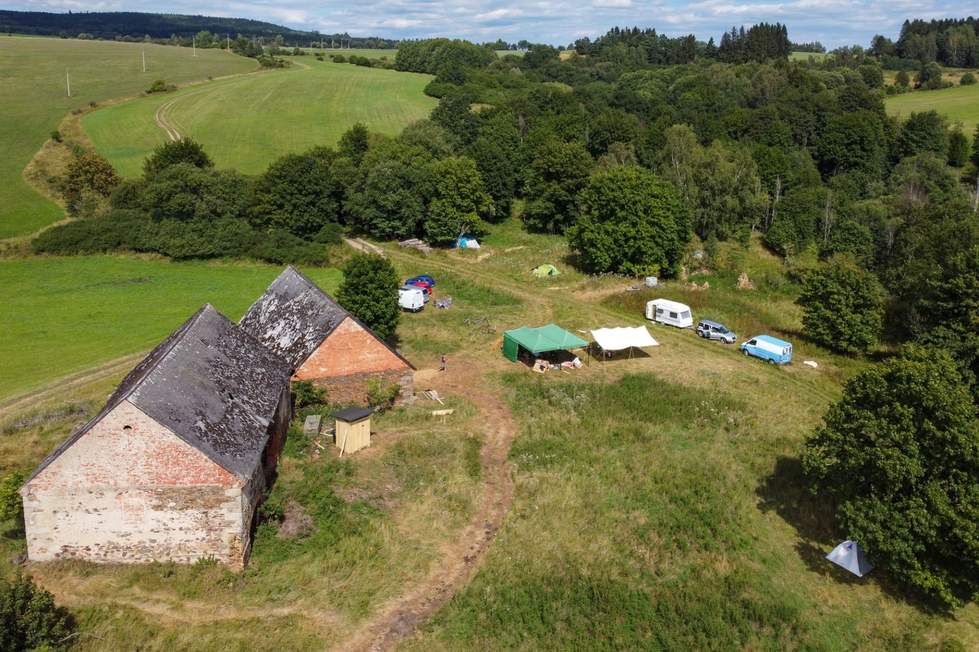 Aerial view of a rural ecovillage with old brick buildings and tents amid green fields.