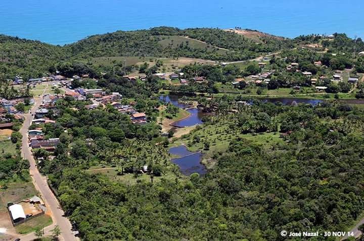 Panoramic view of a tropical ecovillage with houses, water features and surrounding forested hills.