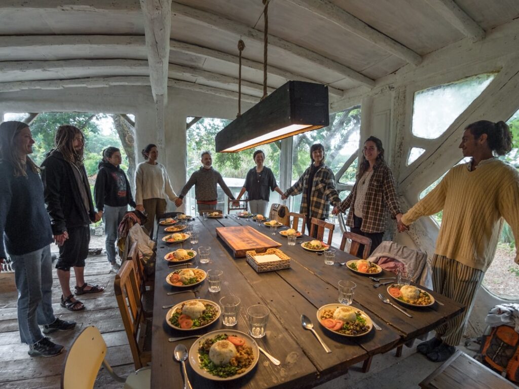 Group of people around a long table with plates of food in a rustic, open-walled setting.