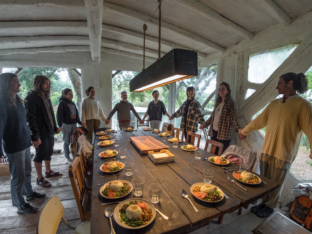 Group of people around a long table with plates of food in a rustic, open-walled setting.