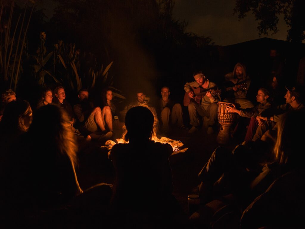 Group of people around a fire circle at night in a garden setting.