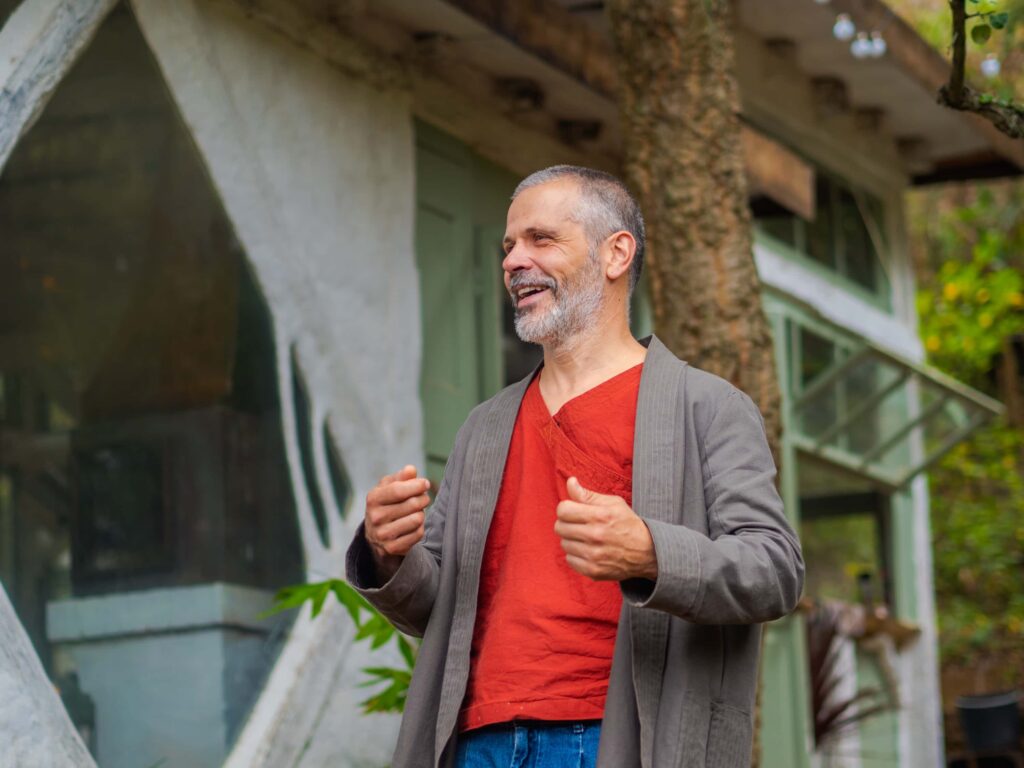 Experienced facilitator in red shirt and grey cardigan speaking outdoors.