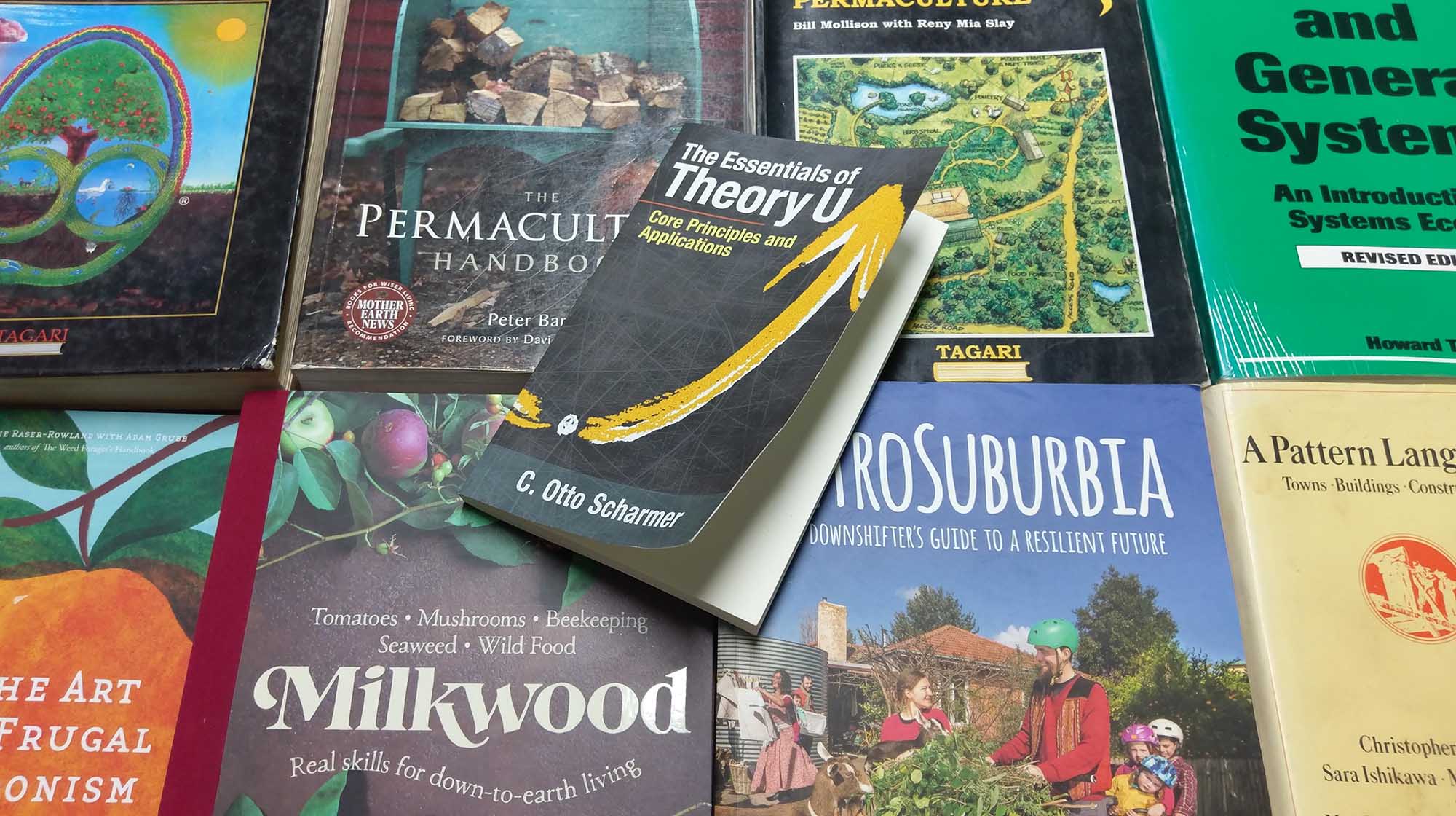 Global Ecovillage Network poster at a bookshelf with permaculture and sustainability titles.