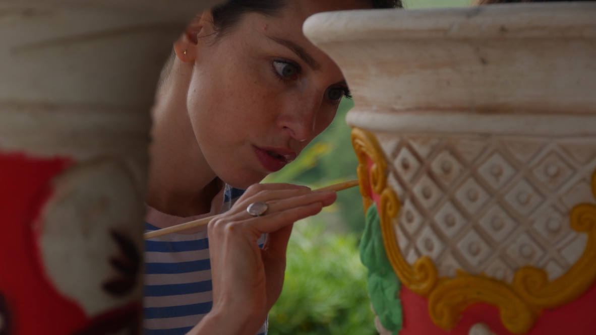 Close-up of a woman applying glaze to a textured clay pot.