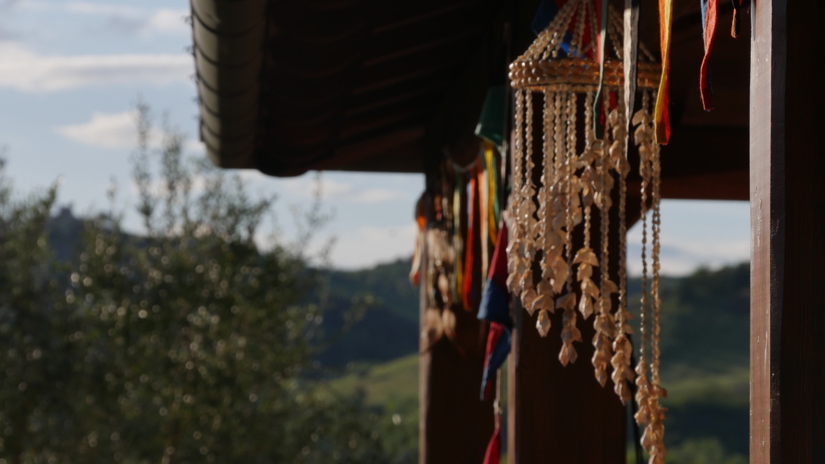 Beaded decorations hanging beside a wooden structure with countryside in the background.