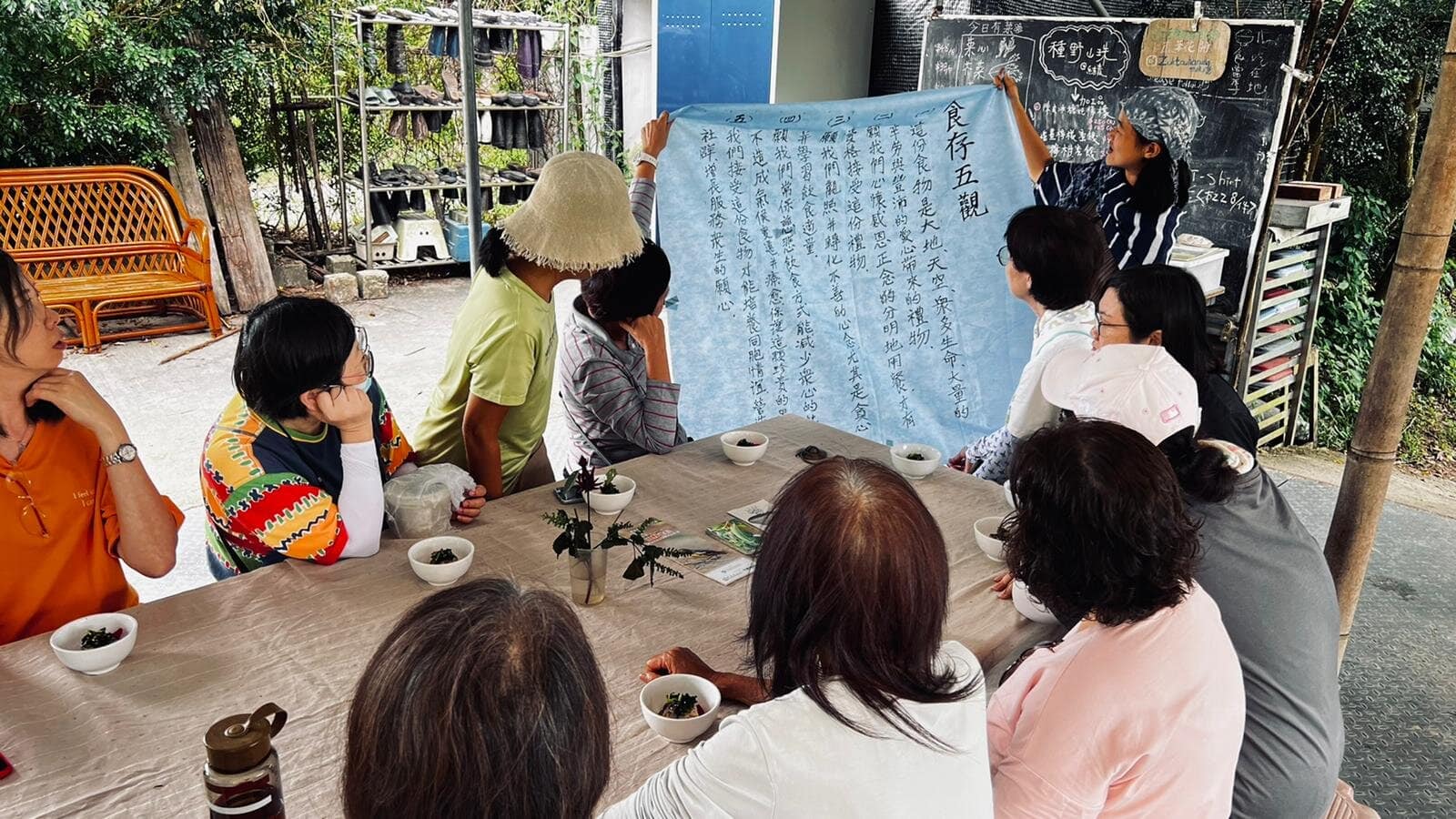 Group of people at an outdoor workshop studying a large blue scroll.
